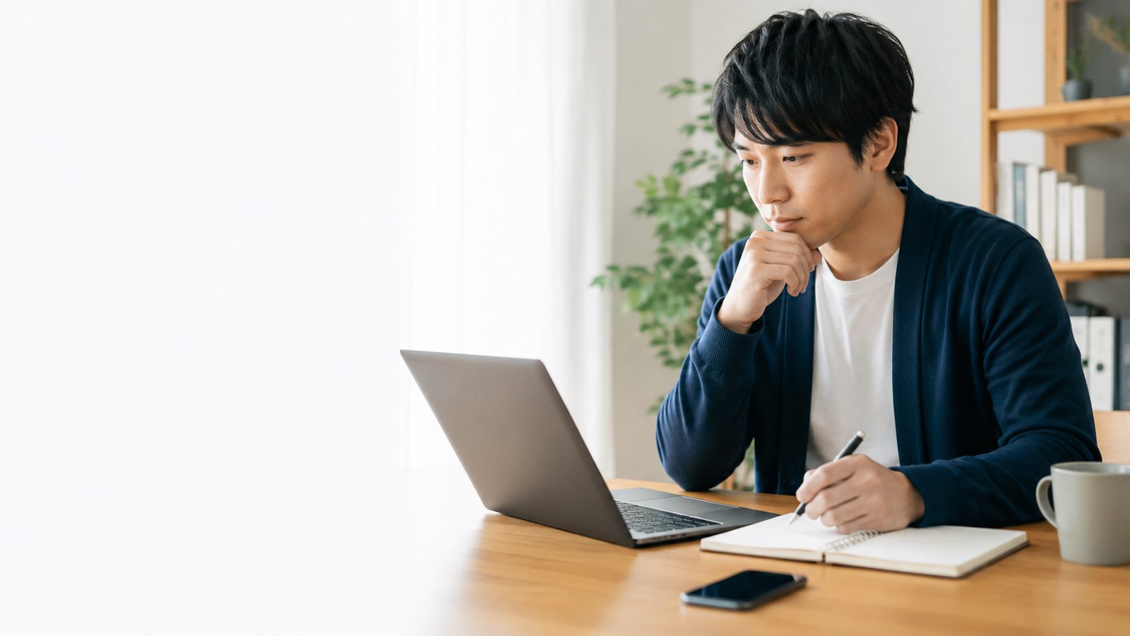 ノートパソコンとノートを使ってAIスクールを比較検討している男性